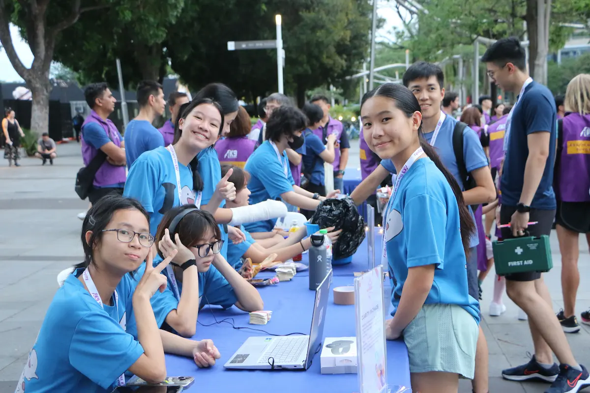An outdoor shot taken at K9 Empawer Walk 2024, of group of student volunteers dressed in blue tees surrounding a table and posing for the camera.